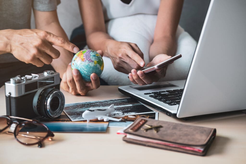 A picture of two people's hands with travel items and looking up a tour on a laptop.